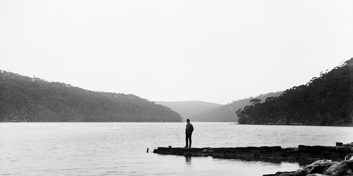 A man standing alone on a small peninsula on a desolate shore. Looks to be from the late 19th century.