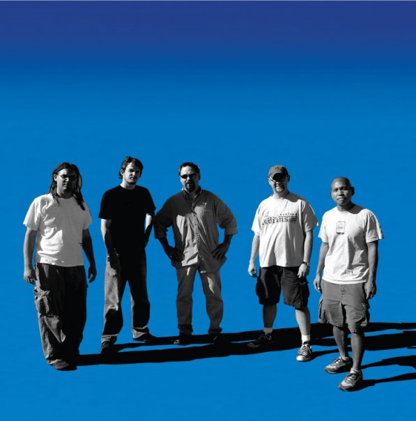 Black and white image of Tim Carmichael, Jon Powers, Gusty Christensen, Doug Carmichael, and Milo Fortes over a blue background. They seem to be staring into the sun which and casts dark shadows behind them.