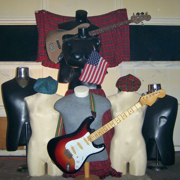 A group of mannequins in garage with a guitar, tartan, and a bass behind them.