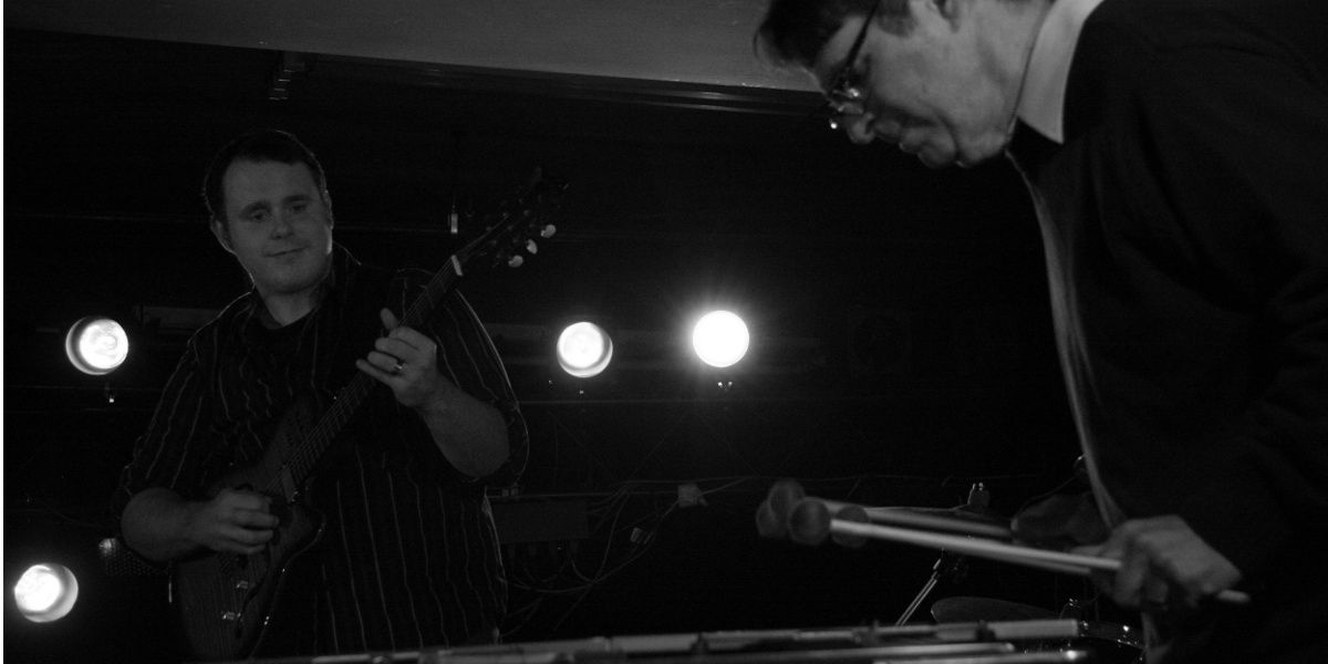 A black and white photo of Pete Ehrmann and Vic Dillahay performing at The Cellar in Longmont, Colorado