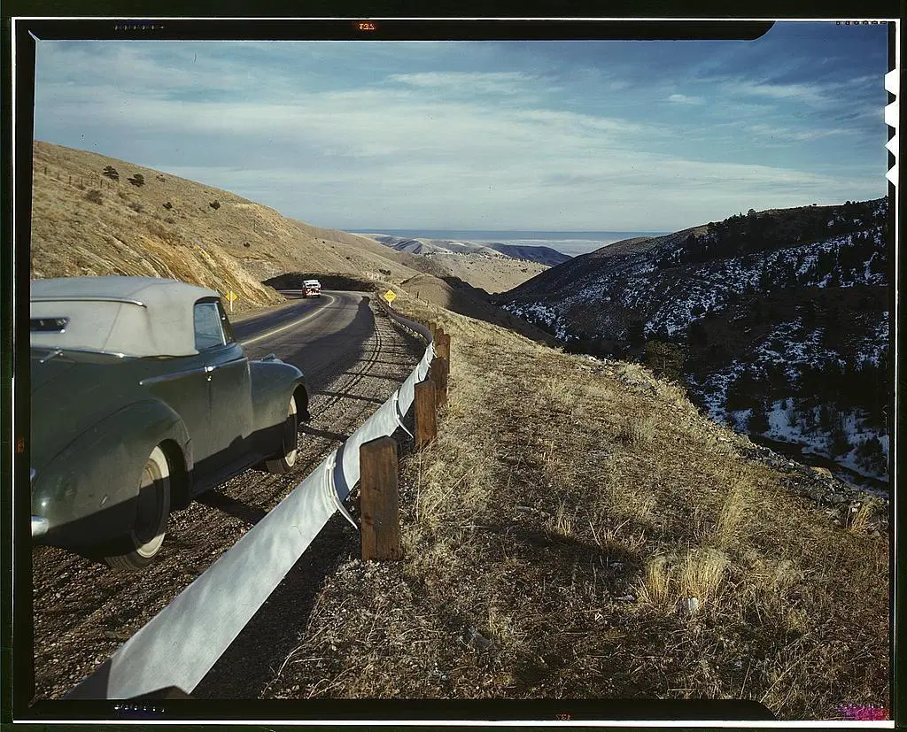 A photo taken in the 1940s of a car on a highway winding down from mountains.