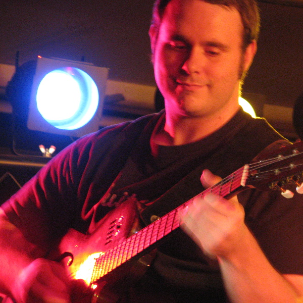 Vic Dillahay with archtop guitar on stage at The Cellar, with stage lights behind.
