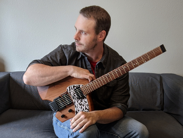 Vic Dillahay sitting on a couch with guitar, in color